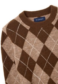 Bruine en beige argyle trui met een klassieke ronde hals. Gemaakt van zachte stof met contrasterende ruitpatronen en witte stiksels.