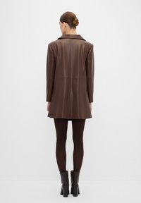 Bruine leren oversized jack met een gestructureerde kraag en achternaden, gecombineerd met bruin leggings en enkellaarsjes met hakken.