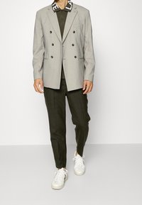 Svetle šedý dvouřadý blazer s klopami, v kombinaci s tmavozeleným polokošilí, dobře padnoucími tmavými kalhotami a bílými teniskami.