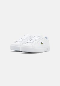 Vita sneakers med en slät syntetisk ovandel, rund tå, snörning framtill, texturerad gummisula och liten grön krokodil-logotyp på sidan.