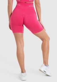 Paarse compressieshorts met een hoge tailleband, een gladde stof en een aansluitend ontwerp, gedragen met witte sneakers.