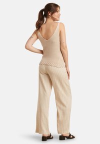 Beige gebreide tanktop met een V-hals, gecombineerd met wijde gestreepte broeken. De stof lijkt lichtgewicht en gestructureerd. Zwarte sandalen maken de look compleet.