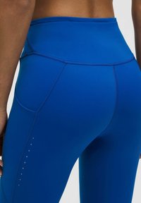 Aukštos juosmens mėlynos leginsai, pagaminti iš lygaus, tamprių audinio. Yra plokščios siūlės ir nedideli dekoratyviniai akcentai šonuose.