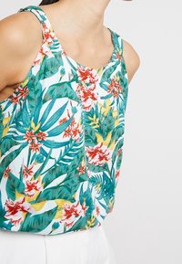 Kukkataulu, jossa on valkoinen pohja, kirkkaan vihreitä lehtiä ja punaisia sekä keltaisia kukkia. Kevyt kangas ja olkaimeton malli.