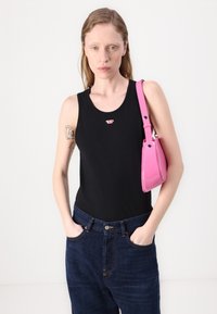 Must Black sleeveless top väike logo, millele on paaritatud kõrge talje sinised teksad. Mudel hoiab läikivat roosat käekotti.