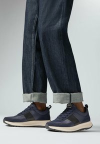 Marineblauwe sportschoenen met zwarte accenten, textuurstof en een rubberen zool. Gecombineerd met opgerolde donkere denimspijkerbroeken.