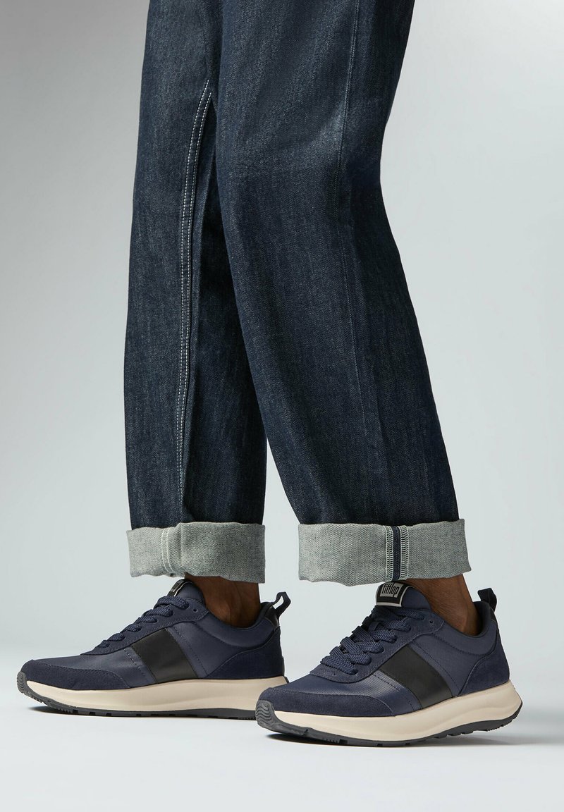 Marineblauwe sportschoenen met zwarte accenten, textuurstof en een rubberen zool. Gecombineerd met opgerolde donkere denimspijkerbroeken.