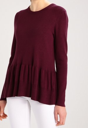 Vinröd långärmad tröja med ribbad rund halsringning och utsvängt volangfåtal. Mjukt stickat tyg med slät textur.