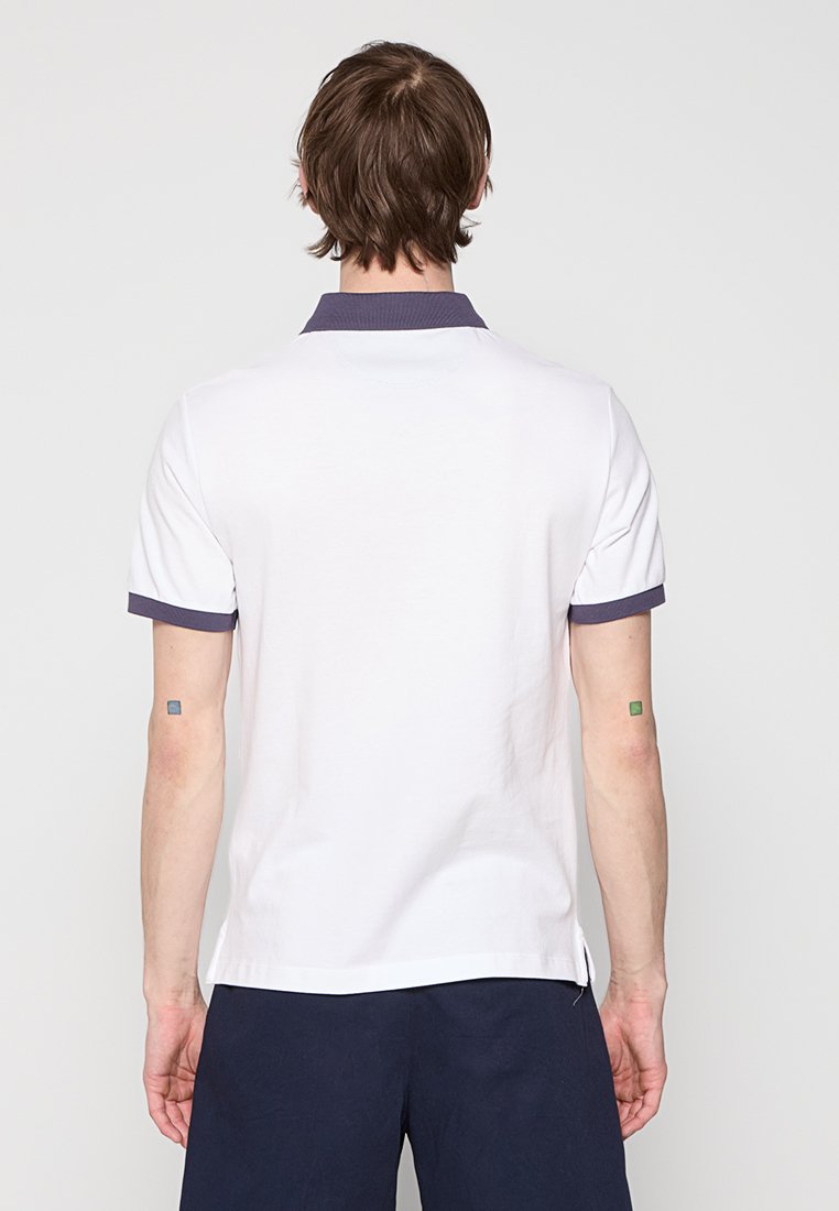 Chemise polo blanche avec un col marine et des accents aux manches, manches courtes et ourlet droit. Tissu en coton avec une texture lisse.