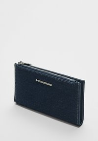 Jeansowy portfel w ciemnoniebieskim kolorze z srebrnym zamkiem błyskawicznym i logo. Charakteryzuje się prostokątnym kształtem i teksturowanym materiałem z kontrastowymi detalami szwów.