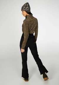 Paita turtleneck kuosisimpukkakuviolla, mustat flared-housut vetoketjuilla lahkeissa ja kuviollinen musta pipo. Pehmeä kangas ja tiukka muotoilu.