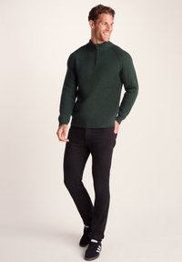 Forest green ribbed knit sweater with half-zip collar, paired with black jeans and black sneakers featuring white stripes. Casual fit.
