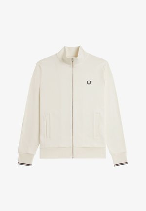 Weiße Jacke mit Reißverschluss und Stehkragen, zwei Fronttaschen, gerippte Bündchen mit schwarzen und roten Streifen sowie ein kleines schwarzes Lorbeerkranz-Logo auf der Brust.