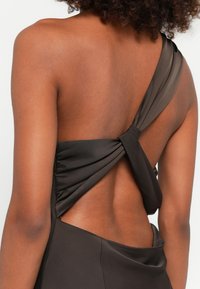Robe à épaule unique en tissu marron foncé, présentant un design de dos torsadé avec une découpe ouverte, une texture lisse et des lignes épurées.