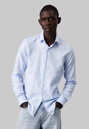 Lichtblauw overhemd met knoopjes, voorzien van een subtiel textuurpatroon, lange mouwen en een klassieke kraag. Gecombineerd met vervaagde denim jeans.