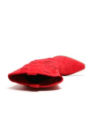 Botín de ante rojo hasta el tobillo con puntera afilada, detalle de bordado floral y superficie texturizada. Suela plana con un tacón delgado.