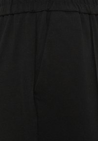 Tissu en coton noir avec une texture lisse et un subtil éclat, taille élastique froncée et silhouette ample avec des plis latéraux.