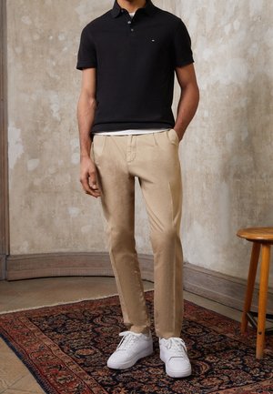 Sort polo-shirt, beige bukser og hvide sneakers. Glat stof med en tætsiddende design. Poloen har en krave og tre knapper.