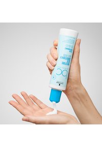 Vochtinbrengende gezichtscrème in een witte tube met een blauwe dop. Romige witte crème die op een open handpalm wordt gedoseerd. Duidelijke merktekst en producttekst zichtbaar.