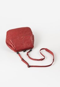 Rode leren rugzak met een ronde vorm, ritsluiting, opbergvak met een knop aan de voorkant en verstelbare schouderband. Gladde textuur met minimale accenten.