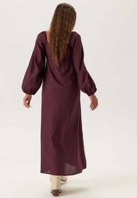 Lungo vestito bordeaux con maniche a sbuffo, corpino aderente e gonna fluttuante. Tessuto liscia con una leggera lucentezza e design semplice.