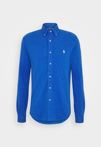 Niebieska koszula zapinana na guziki z kołnierzykiem, długimi rękawami i białymi guzikami. Zawiera małe białe logo po lewej stronie klatki piersiowej. Wykonana z miękkiego materiału.