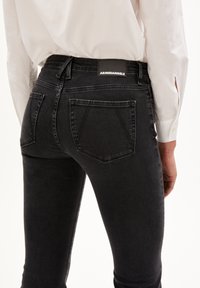 Black denim high-waisted jeans with a fitted silhouette, featuring back pockets, subtle stitching details, and a logo patch on the waistband.