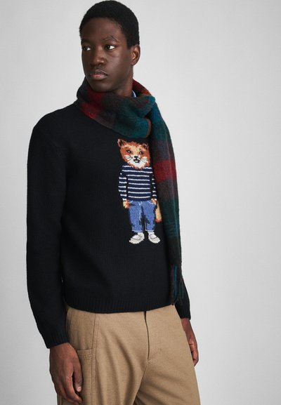 Pull en maille noir avec un graphique de renard sur une chemise rayée, associé à une écharpe en tartan multicolore avec des accents verts, rouges et bleu marine.