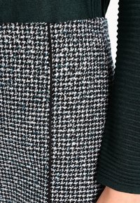 Vävd kjol med svart och vit rutig mönster, med teal-accenter. Texturerad stickad midjeband och detaljer vid sidansöm.