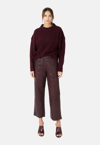 Bordeaux oversized trui met een ronde halslijn, gecombineerd met high-waisted bordeaux leren broeken en open-toed bordeaux hakken.
