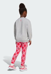 Gray sweatshirt with a circular design, paired with pink leggings featuring large red polka dots and cartoon character accents. Pink sneakers with stripes.