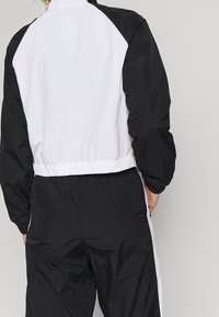 Svart och vit vindjacka med avslappnad passform, elastisk midja och ärmslut. Tillverkad av lätt, rynkat tyg, med raglanärmar.