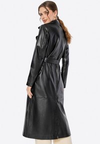 Cappotto trench nero in pelle con vita s cinturato, maniche lunghe e design con spacco sul retro, che mostra una texture liscia e lucida.