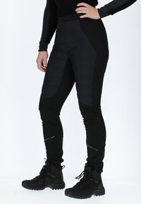Schwarze isolierte Hosen mit strukturierten Einsätzen, schmaler Schnitt, elastisches Material und kontrastierende Akzente. Kombiniert mit schwarzen Wanderschuhen.