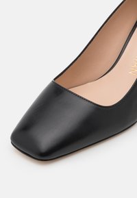 Chaussure plate femme en cuir noir à bout pointu, finition lisse et doublure intérieure beige sur fond blanc.