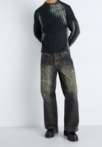 Mörkgrön ribbad stickad tröja med rund halsringning, kombinerad med lösa svarta jeans med en slitna finish och synlig sömnad. Svarta platåstövlar.