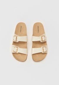 Sandal med cremet farve, to justerbare stropper og accentueret med guldfarvet hardware. Blødt tan indlæg med en glat, blank overflade.