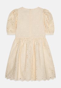 Robe beige clair avec des manches bouffantes, motif floral brodé et détails découpés. Ourlet évasé et fermeture à clé au dos.