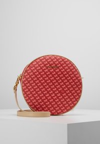 Okrągła torba w czerwono-czarny wzór houndstooth, wykonana z teksturowanego materiału, z beżowym paskiem i złotymi akcesoriami. Logo wyeksponowane w widoczny sposób.