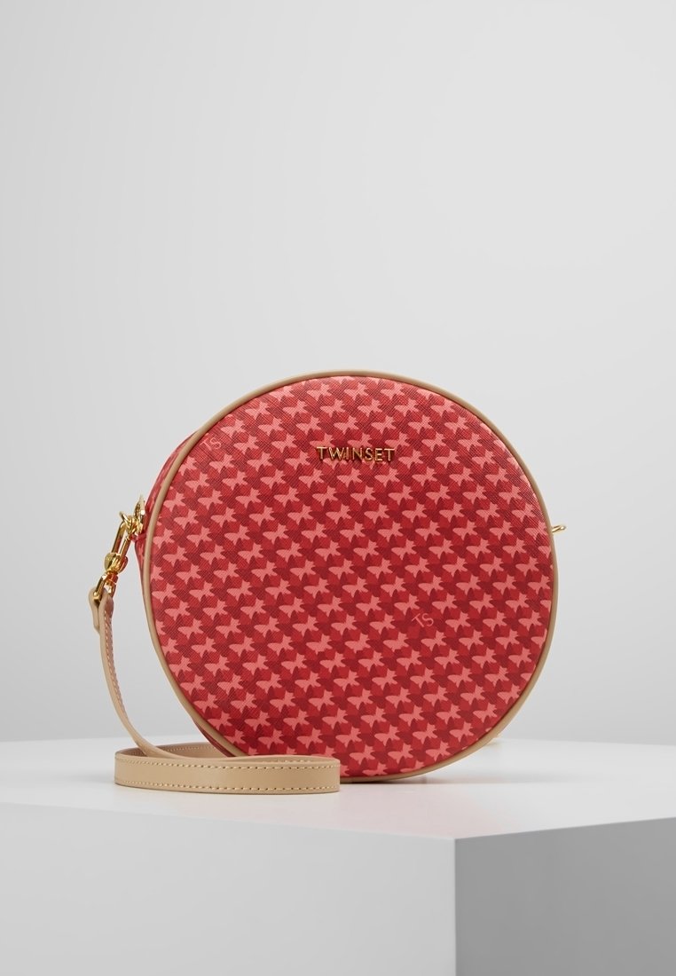 Okrągła torba w czerwono-czarny wzór houndstooth, wykonana z teksturowanego materiału, z beżowym paskiem i złotymi akcesoriami. Logo wyeksponowane w widoczny sposób.