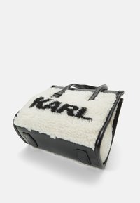 Sac en cuir noir avec un devant en fourrure synthétique crème portant le mot "KARL" en noir. Forme rectangulaire avec des poignées de transport doubles.