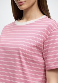 Ροζ κοντομάνικη μπλούζα με λευκές οριζόντιες ρίγες, στρογγυλή λαιμόκοψη και απαλό βαμβακερό ύφασμα. Διαθέτει κοντράστ γιακά ως λεπτομέρεια.
