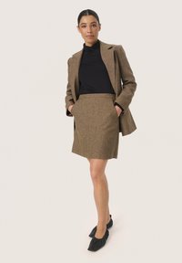 Blazer en tweed marron avec revers crantés, col roulé noir, jupe marron assortie et ballerines noires avec des accents froncés. Design simple et structuré.