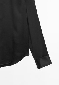 Black long-sleeve shirt featuring a smooth texture, rounded hem, and satin cuff accents. Fabric appears lightweight and fluid.