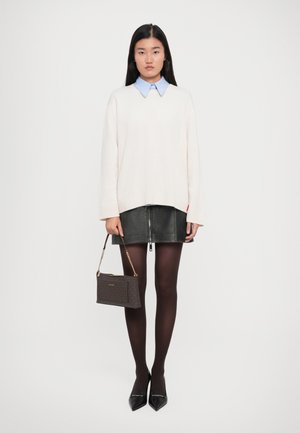 Donna che indossa un maglione bianco sopra una camicia azzurra con colletto, una minigonna di pelle nera, collant scuri e tacchi neri, mentre tiene una borsa di design marrone di lato.