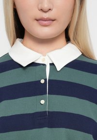 Groene en marineblauwe gestreepte polo met een witte kraag, voorzien van een knoopsluiting en een zachte textuur. Gedetailleerde stiksels en scherpe lijnen.