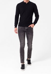 Pull en maille noir avec un motif en losange, col et manches longues, associé à un jean slim gris foncé et des baskets noires.