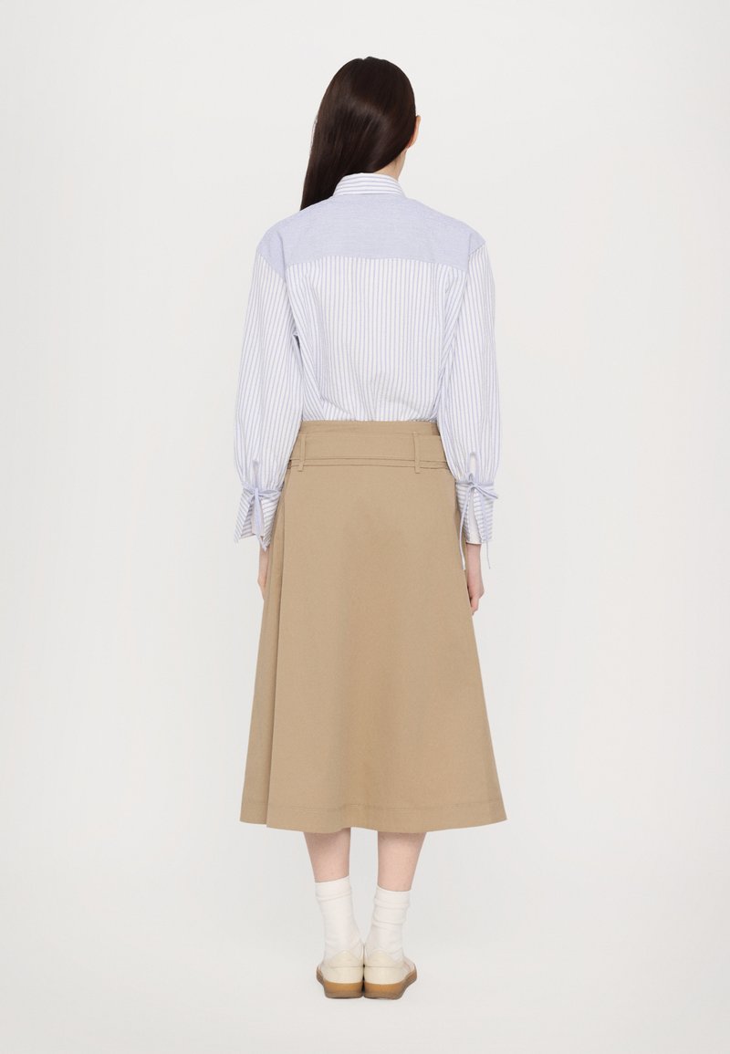 Chemise rayée bleu clair avec des manches retroussées, associée à une jupe beige à la longueur des genoux en forme de A. Chaussettes blanches à la cheville et chaussures marron.