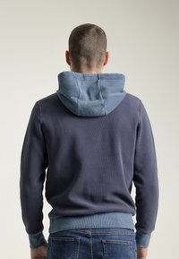 Sudadera con un cuerpo azul marino oscuro y capucha y puños de canalé en azul claro. Presenta un tejido texturizado con costuras visibles en la capucha.