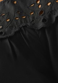 Czarna tkanina z teksturowanym haftowanym kołnierzem, który ma wycięcia i faliste krawędzie, tworząc warstwowy, trójwymiarowy efekt.